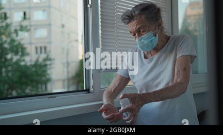 Vieille femme 90 ans portant un masque de visage utiliser l'alcool spray protéger Covid 19 debout par fenêtre dans la maison de soins, rester à la maison, concept de soins de santé, nouveau Banque D'Images