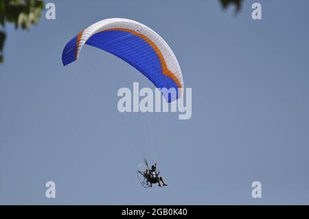 Parapente avec une hélice sur son dos volant au-dessus de l'eau bleue avec des nageurs. Banque D'Images