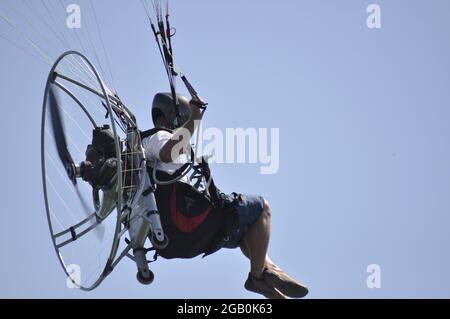 Parapente avec une hélice sur son dos volant au-dessus de l'eau bleue avec des nageurs. Banque D'Images