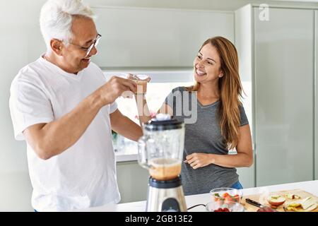 Couple hispanique d'âge moyen souriant bon verre de smoothie à la cuisine. Banque D'Images