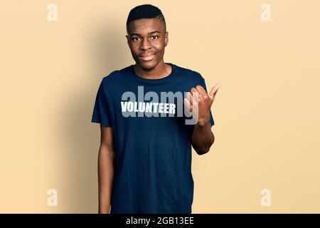 Un jeune homme afro-américain portant un t-shirt de volontaire pointant vers le dos avec la main et les pouces vers le haut, souriant confiant Banque D'Images