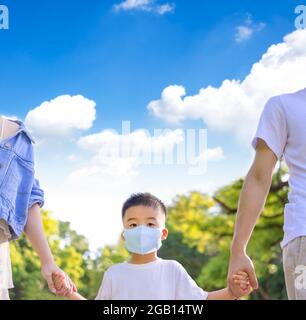 Garçon portant le masque médical et parent marchant dans le parc. Banque D'Images