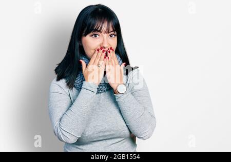 Jeune femme hispanique de taille plus portant un foulard d'hiver riant et Giggle embarrassé couvrant la bouche avec les mains, les potins et le concept de scandale Banque D'Images