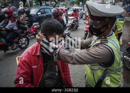 Makassar, Sulawesi du Sud, Indonésie. 2 août 2021. Un policier commande un masque pour un automobiliste qui passe lors d'un raid sur un protocole de santé à la frontière de la ville de Makassar et de Gowa Regency, en Indonésie. Un par un, les conducteurs qui ne portaient pas de masques ont été arrêtés et invités à porter des masques. L'inspection a été effectuée dans le cadre d'une série de mesures de restriction des activités communautaires de niveau 4 (PPKM) dans la ville de Makassar afin de supprimer la propagation de Covid-19 qui continue d'augmenter. (Image de crédit : © Herwin Bahar/ZUMA Press Wire) Banque D'Images