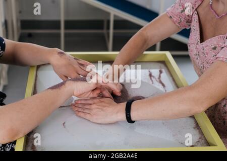 Les enfants ayant un handicap se font une activité sensorielle plateau de sable, table de sable pour l'animation, infirmité motrice cérébrale jouant au jeu apaisant, entraînement moteur fin Banque D'Images