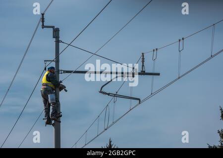 Peintres ou ouvriers d'entretien réparant des poteaux électriques ou caténaires pour l'électricité sur une ligne de chemin de fer ou de chemin de fer. Travailleur unique sur les poteaux Banque D'Images