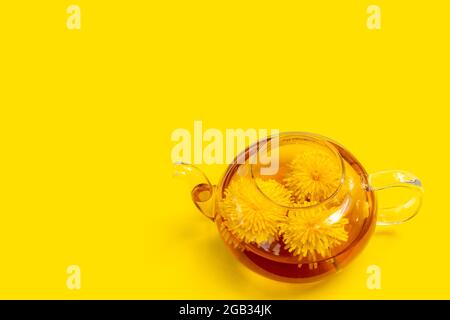Théière transparente en verre avec thé à base de plantes saines à base de pissenlits jaunes sur fond jaune. Boisson écologique à base de plantes, Banque D'Images