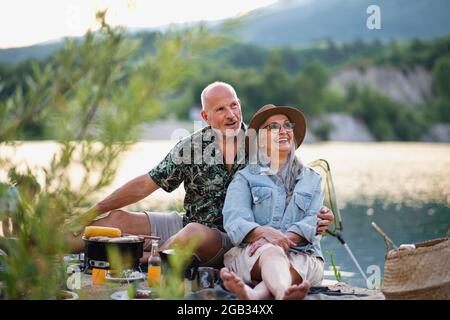 Couple senior heureux se reposant sur les vacances d'été, barbecue au bord du lac. Banque D'Images