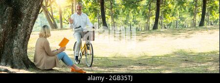 une femme âgée assise sur un automne tombé laisse lire un livre. dans un parc et attendant le vélo de mari ou d'ami Banque D'Images