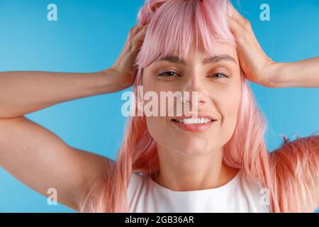 Gros plan portrait d'une belle mannequin avec des cheveux roses souriant à l'appareil photo tout en posant isolé sur un arrière-plan de studio bleu Banque D'Images