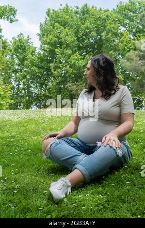 Femme enceinte assise sur l'herbe et posant heureusement Banque D'Images