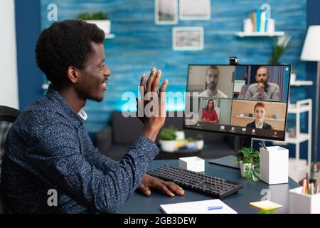 Homme afro-américain en ligne de conférence vidéo avec des collègues de travail utilisant la communication par webcam. Travailleur Internet à distance travaillant à domicile en gardant la distance tout en utilisant la technologie Banque D'Images