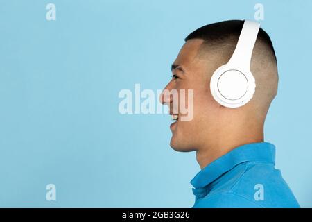 Vue latérale. Portrait d'un jeune homme asiatique souriant dans un casque blanc isolé sur un fond bleu clair de studio. Banque D'Images