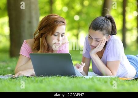 Deux étudiants se sont concentrés e-learning avec ordinateur portable et des notes sur l'herbe dans un campus Banque D'Images