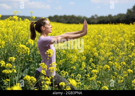 Profil d'une femme faisant de l'exercice de tai chi debout dans un champ jaune Banque D'Images