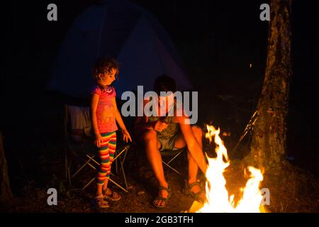 Papa et fille s'assoient la nuit près du feu en plein air en été dans la nature. Voyage de camping en famille, rassemblements autour du feu de camp. Fête des pères, Banque D'Images