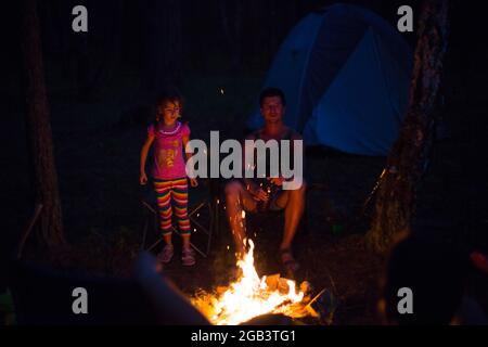 Papa et fille s'assoient la nuit près du feu en plein air en été dans la nature. Voyage de camping en famille, rassemblements autour du feu de camp. Fête des pères, Banque D'Images