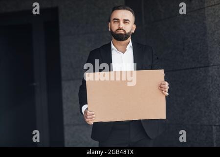 Homme d'affaires mature protestant contre le verrouillage dans la rue, montrant un panneau de carton vide, mockup pour votre texte Banque D'Images