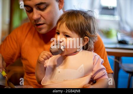 un adorable tout-petit aime manger de la glace à la popsicle sur les genoux de ses parents Banque D'Images