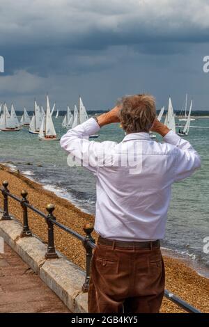 homme regardant à travers des jumelles, semaine des cowes, régate de course de yacht, régate de voile, homme spectateur, homme regardant des courses de yacht, homme observant des bateaux de voile. Banque D'Images