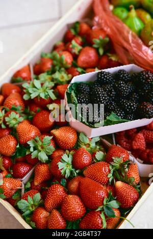 Boîte avec des boîtes de fraises, framboises, figues et mûres se trouve sur une tuile Banque D'Images