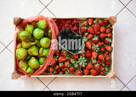 Un kit en bois avec des boîtes de fraises, framboises, figues et mûres se trouve sur un carreau léger Banque D'Images