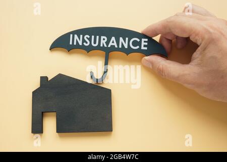 Concept d'assurance habitation. La main tient un parapluie au-dessus de la maison. Banque D'Images