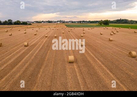 Un champ avec des balles de foin après la récolte avec une vue d'autres champs et un village en contre-jour Banque D'Images