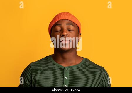 Portrait de l'homme noir calme debout avec les yeux fermés sur fond jaune Banque D'Images
