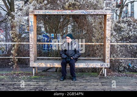 Homme âgé âgé âgé en vêtements d'hiver assis sur un banc, qui a l'air triste et attentionné. Banque D'Images