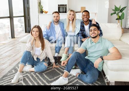 Portrait d'amis multiraciaux joyeux assis dans le salon, regardant l'appareil photo et souriant Banque D'Images