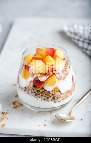 Yaourt à la granola avec pêche dans un verre. Nourriture de dessert saine faible en calories Banque D'Images