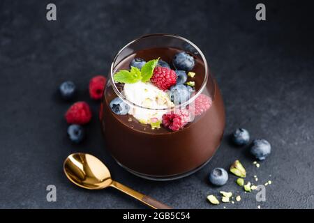 Mousse au chocolat noir avec pistaches, baies et crème en pot, fond de pierre noire, vue rapprochée Banque D'Images
