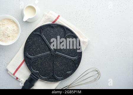 Poêle à frire vide noire, poêle avec revêtement antiadhésif en pierre pour cuire des crêpes en forme de coeur de petit déjeuner et des ingrédients sur la table en béton gris Banque D'Images