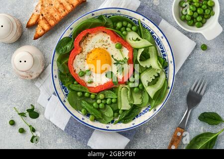 Poivrons rouges farcis avec des œufs, des feuilles d'épinards, des pois verts et des microverts sur une assiette de petit déjeuner sur fond de table gris clair. Vue de dessus. Banque D'Images