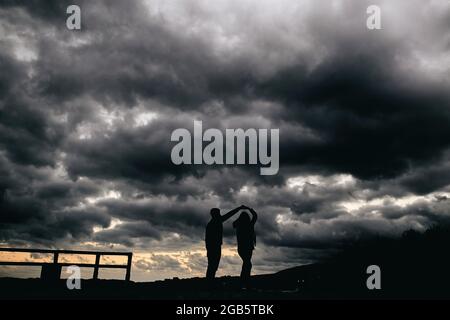 Silhouette d'un jeune couple dansant au coucher du soleil avec une tempête en arrière-plan Banque D'Images