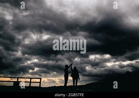 Silhouette d'un jeune couple dansant au coucher du soleil avec une tempête en arrière-plan Banque D'Images