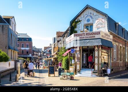 Les touristes se baladent dans la rue Monge à Etretat, en France, bordée de bâtiments typiques, de cafés-terrasses et de boutiques de cadeaux par temps ensoleillé. Banque D'Images