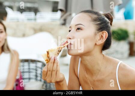 Portrait en gros plan d'une heureuse femme asiatique américaine qui mange de la pizza. Banque D'Images