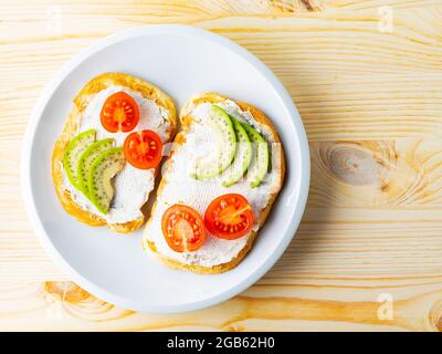 Deux toasts avec avocat et tomates cerises sur fond de bois. Toasts d'avocat avec fromage à la crème sur une assiette blanche. Copier l'espace. Vue de dessus Banque D'Images