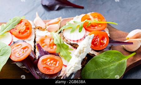 Bruschetta italienne avec fromage à la crème et herbes fraîches. Bruschetta au fromage à la crème, tomates cerises et ail sur une planche à découper. Gros plan Banque D'Images