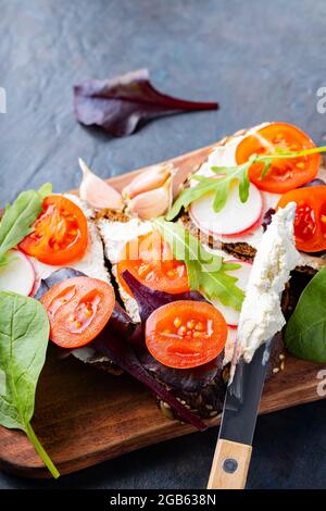 Bruschetta italienne avec fromage à la crème et herbes fraîches. Bruschetta au fromage à la crème, tomates cerises et ail sur une planche à découper. Gros plan Banque D'Images