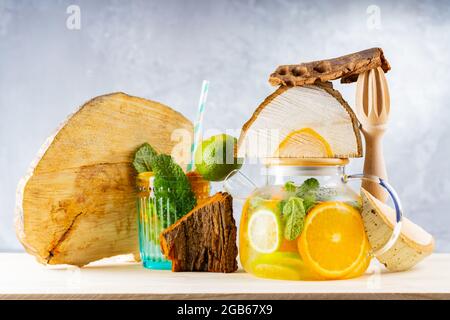 Limonade boire de l'eau, du citron, de l'orange et des feuilles de menthe dans une théière transparente. Thé glacé à la menthe et morceaux de bois. Composition créative Banque D'Images