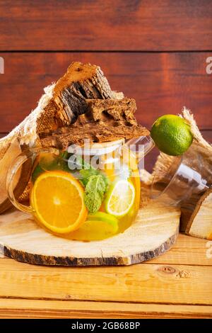 Boisson estivale d'eau, de citron, d'orange et de feuilles de menthe sur des planches de bois. Thé glacé à la menthe et morceaux de bois. Composition créative Banque D'Images