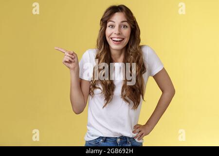 Vif surpris heureux enthousiaste bonne-look femme long bouclés T-shirt blanc rire impressionné étonné pointant l'index gauche Banque D'Images