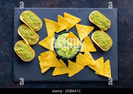 Sauce guacamole mexicaine avec des chips de nachos sur un plateau d'ardoise. Croustilles tortilla et guacamole sur fond sombre. Copier l'espace. Vue de dessus Banque D'Images