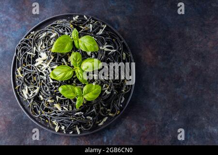 Pâtes noires au fromage râpé et au basilic sur fond sombre. Spaghetti noirs avec de l'encre de seiche sur une assiette noire. Pâtes avec parmesan et fres Banque D'Images