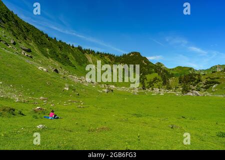 Randonneur sur le chemin dans la grande vallée de Walser. paysage alpin avec des roses alpines et d'autres fleurs alpines, des sapins et des montagnes. Klesenzaalpe Banque D'Images