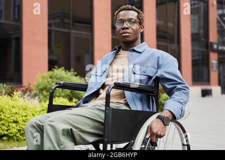 Jeune homme afro-américain pensif avec des jambes paralysées en fauteuil roulant tout en étant sur la promenade Banque D'Images