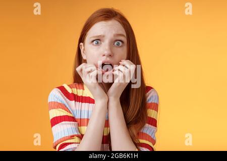 Timid non sécurisé jeune fille gingembre yeux bleus se sentant effrayé souffle peur secouée choquée peur tenir les doigts bouche frognant grimaçant la regarder Banque D'Images